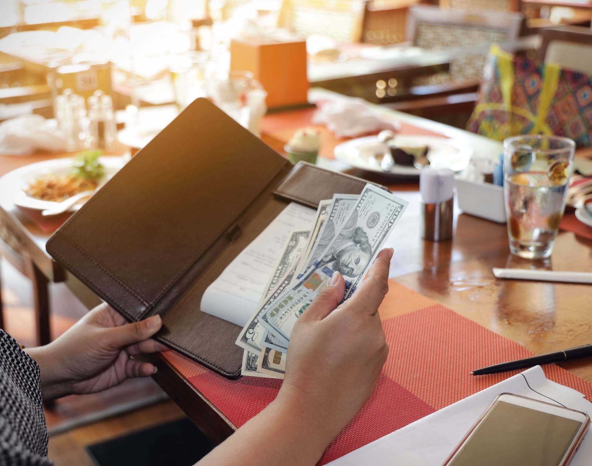 Woman placing American $20 bills into a restaurant check folio, representing restaurant tax
