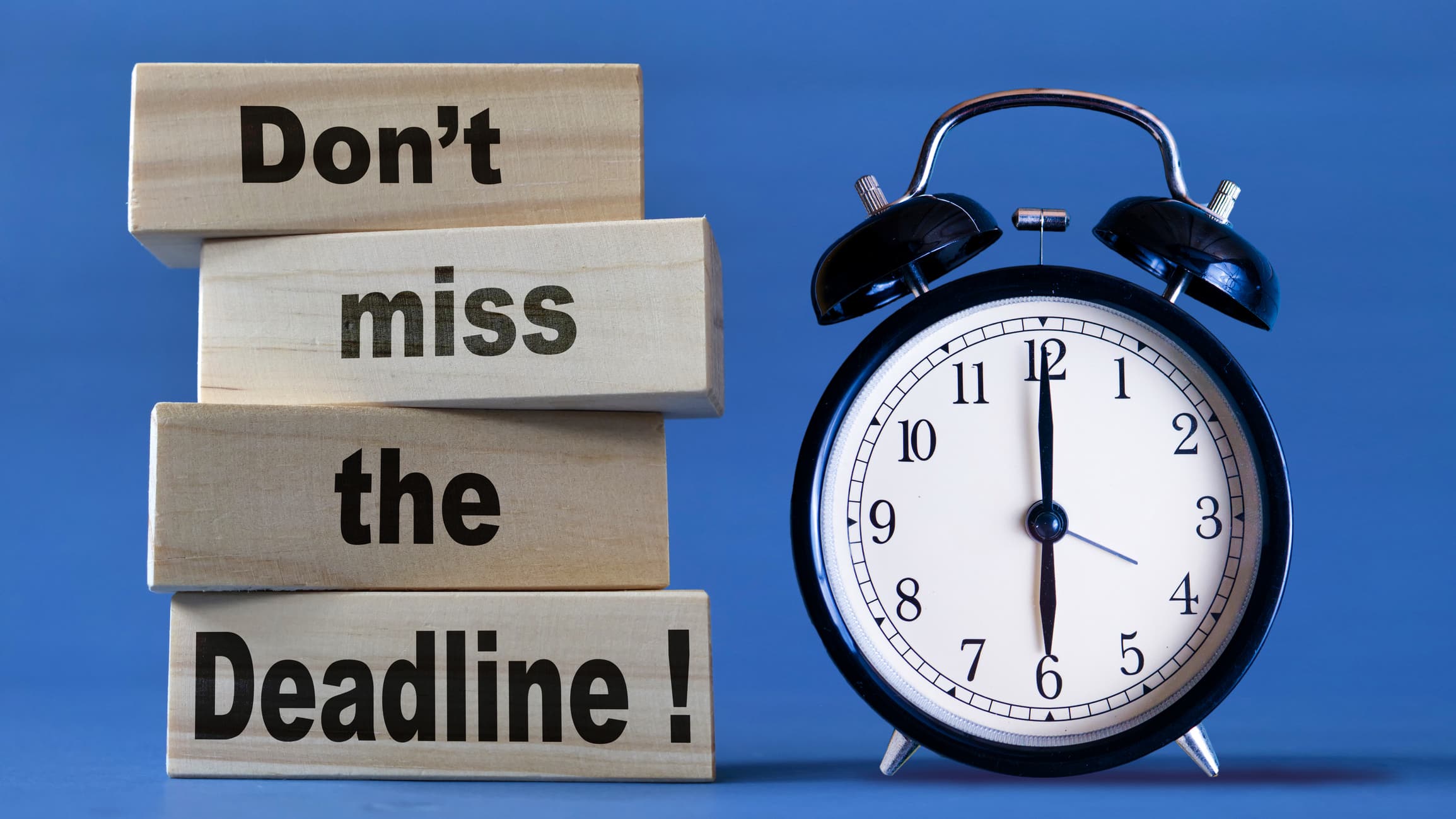 Analog alarm clock next to stacking blocks that say Don't miss the deadline.
