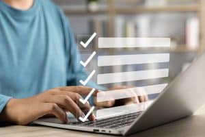 person in a blue shirt sitting in front of a laptop with a checklist overlay
